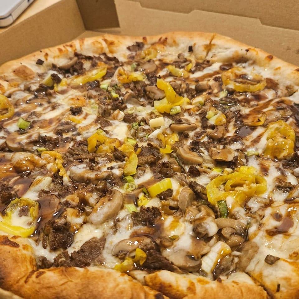 Loaded pizza with mushrooms, ground meat, melted cheese, and sliced yellow peppers in an open cardboard box.